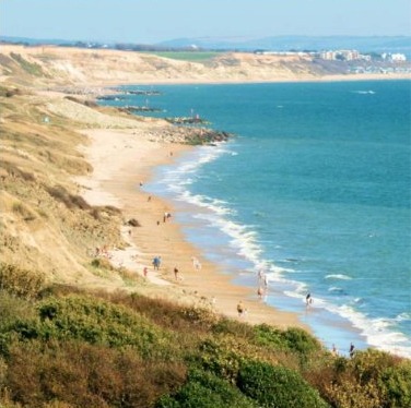 Long sandy beach curving along a turquoise coastline seen from a grassy clifftop