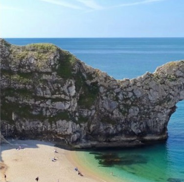 Durdle Door rock arch above a sandy beach and clear blue water
